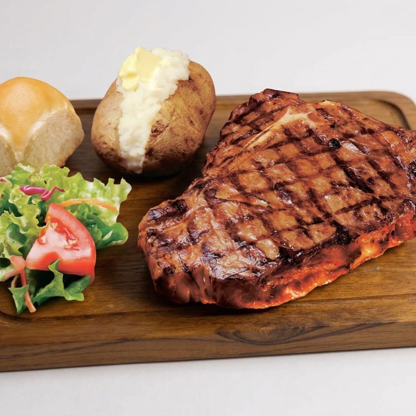 Grilled steak with a baked potato, butter, dinner roll, and side salad on a wooden board.