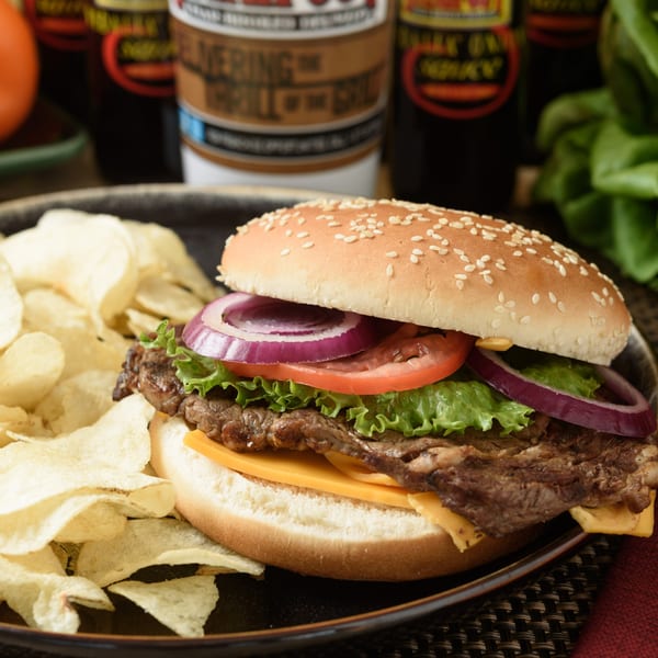 Grilled steak sandwich with cheese, lettuce, tomato, and onion, served with potato chips.