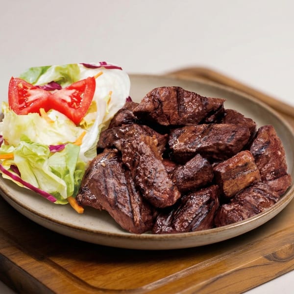 Plate of grilled steak bites with a side salad of lettuce, shredded carrots, and tomato.