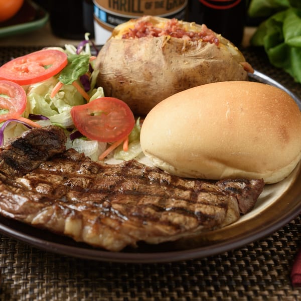 Grilled steak, baked potato with bacon, side salad, and a dinner roll on a plate.