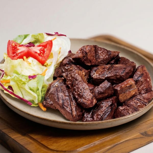 Grilled steak bites with a side salad of lettuce, shredded carrots, red cabbage, and tomato.