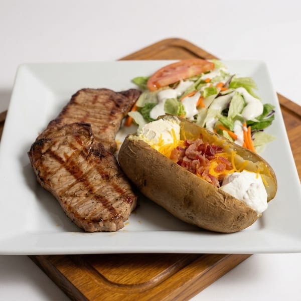 Grilled steak, loaded baked potato with bacon and cheese, and a side salad on a white plate.