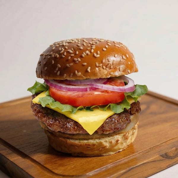 A delicious cheeseburger with lettuce, tomato, and red onion on a sesame seed bun.