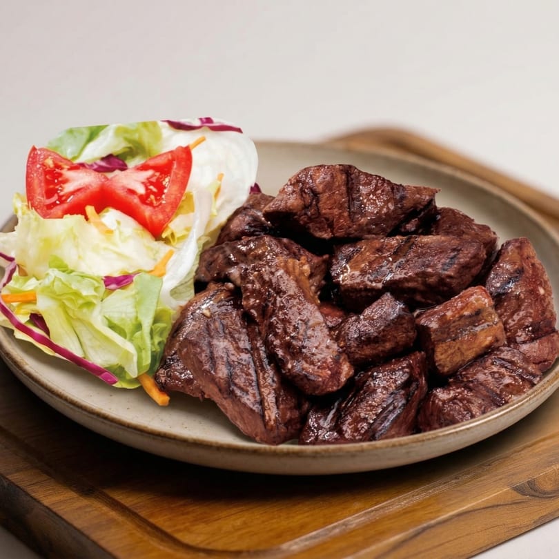 Grilled beef cubes with a side salad of lettuce, shredded carrots, red cabbage, and tomato.