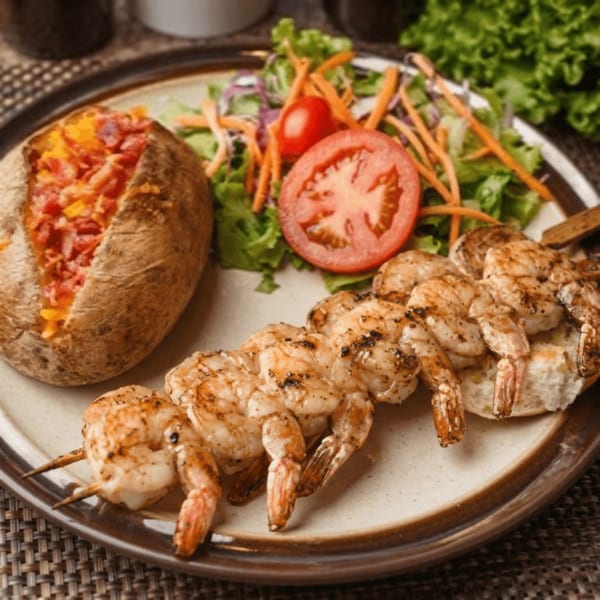 Grilled shrimp skewers, a loaded baked potato, and a fresh side salad on a plate.